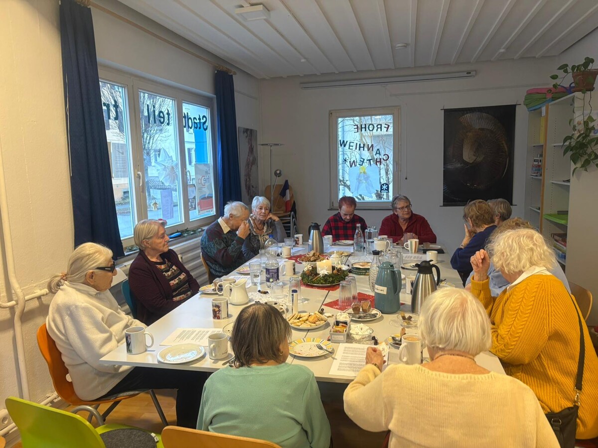 großer Tisch mit vielen Leuten, die zusammen Kaffee trinkem